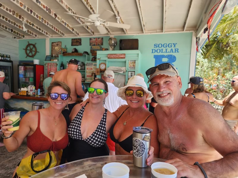Four people in swimwear smiling and holding drinks at a beach bar.