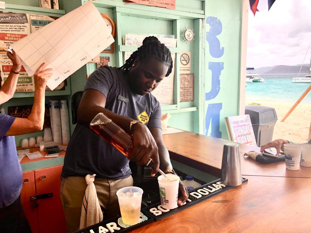 Bartender pouring rum at a beach bar with ocean view in the background.