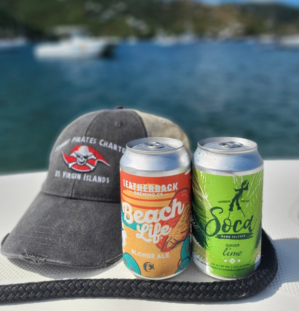 Hat and two drink cans on a boat with water and hills in the background.