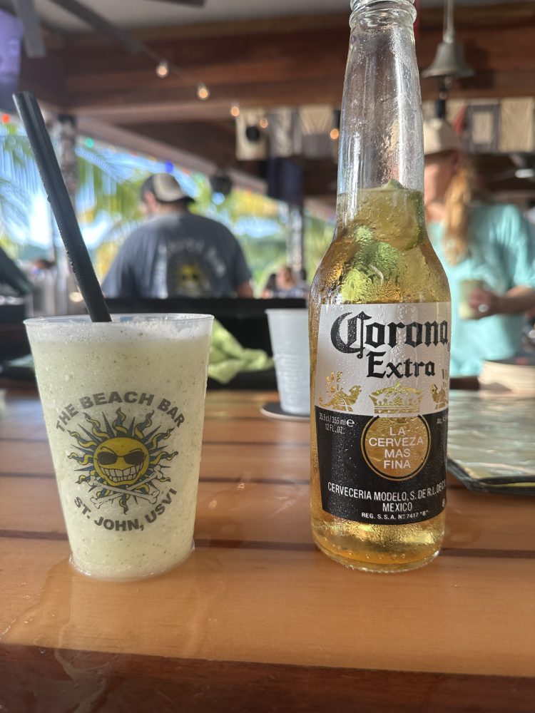 Frozen drink and Corona beer on a wooden bar with people in the background.