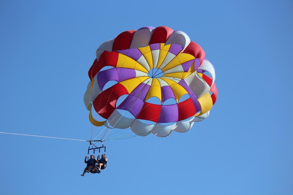 Two people parasailing with a colorful parachute against a clear blue sky.