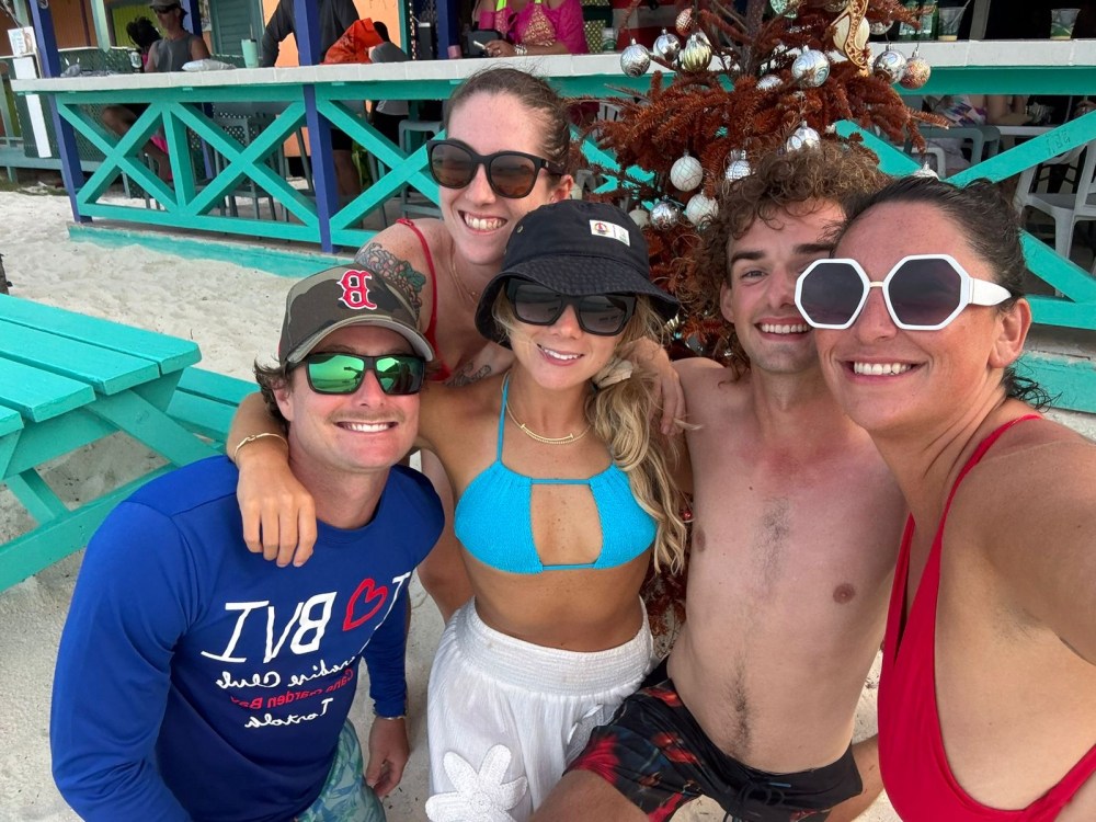 Group of five friends smiling at the beach with festive decorations in the background.