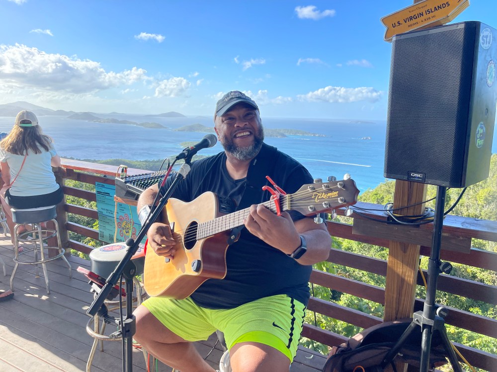 Person playing guitar and singing on a deck with an ocean view.