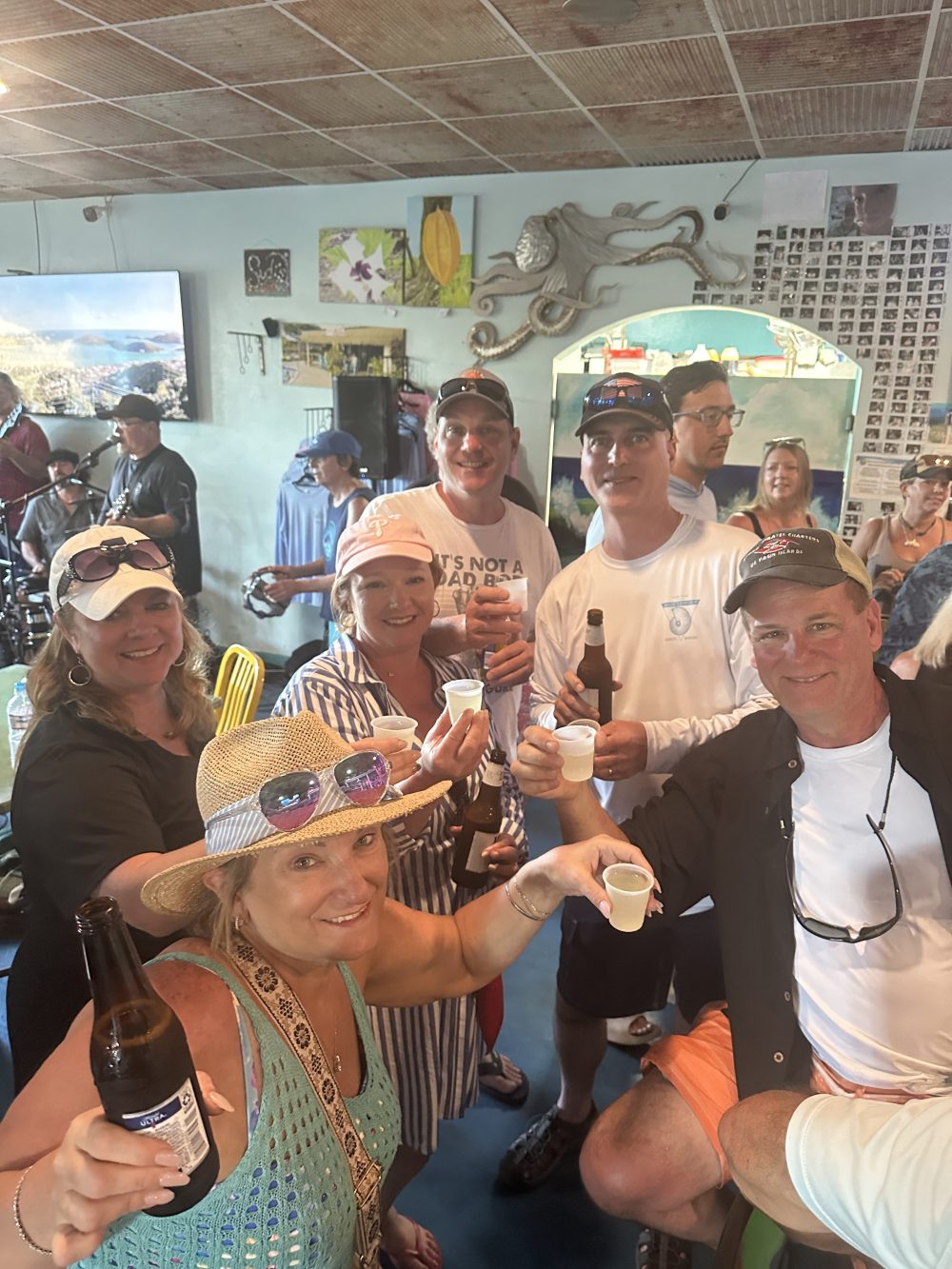 Group of people in a bar holding drinks, smiling at the camera.