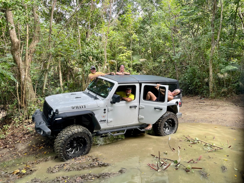 Jeep in muddy forest path with people enjoying adventure