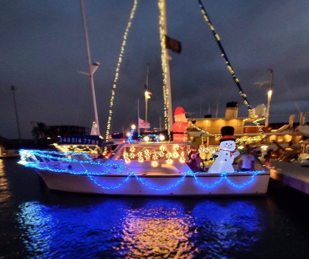 Boat decorated with festive lights and inflatable snowman at night.