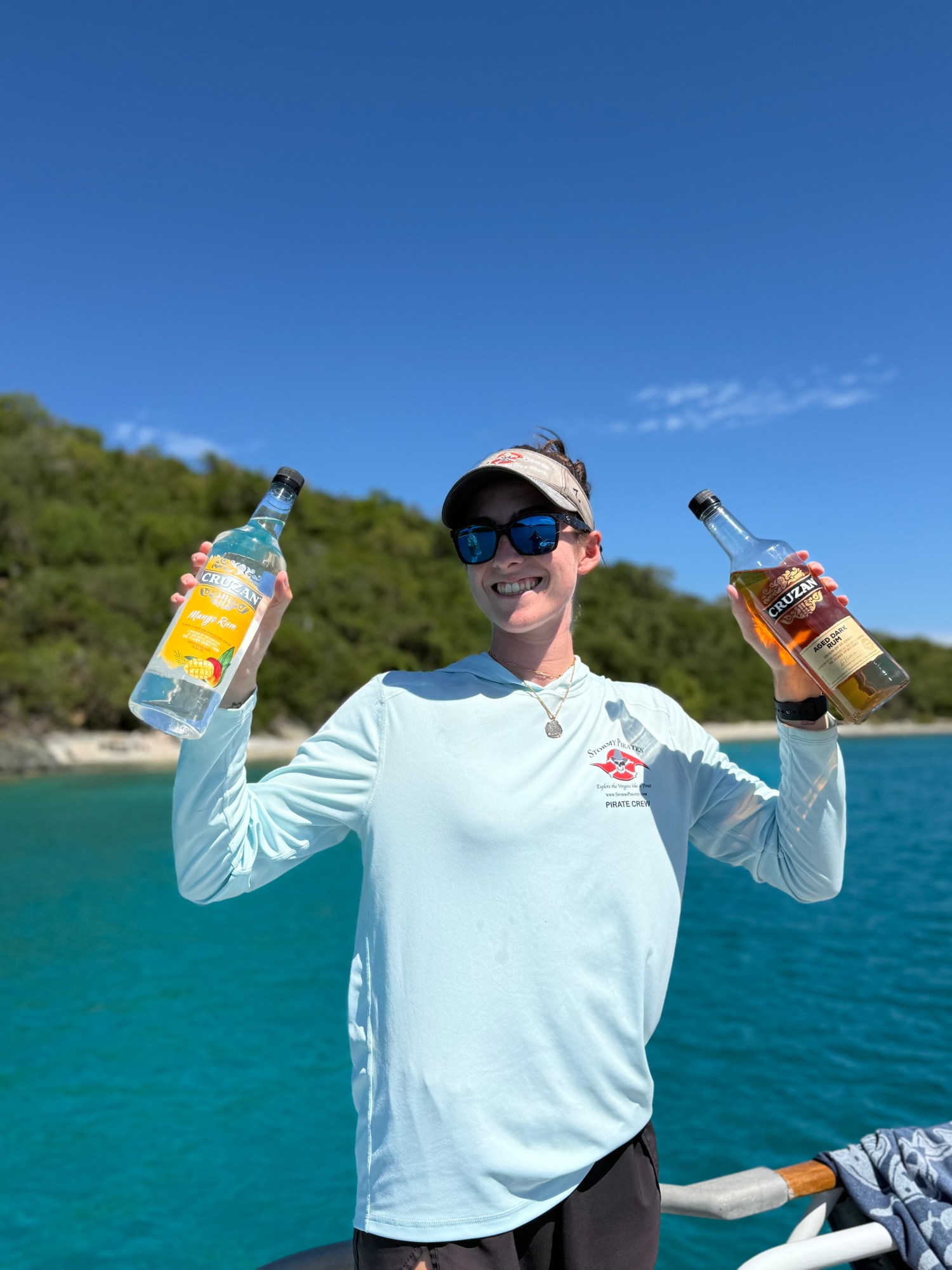 Person on a boat holding two bottles, smiling under a clear blue sky.