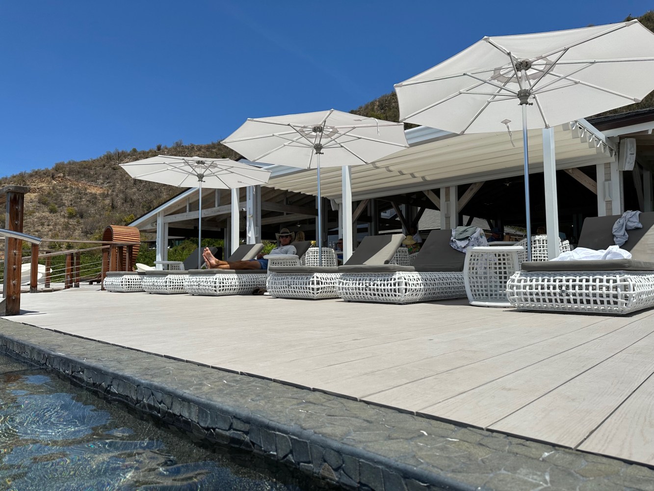 Poolside loungers and umbrellas on a wooden deck with a scenic mountain view.