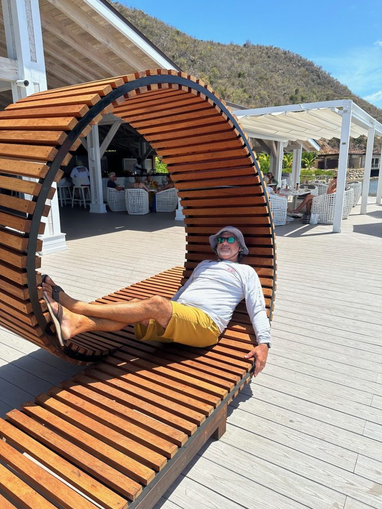 Person relaxing on curved wooden bench in sunny outdoor setting.