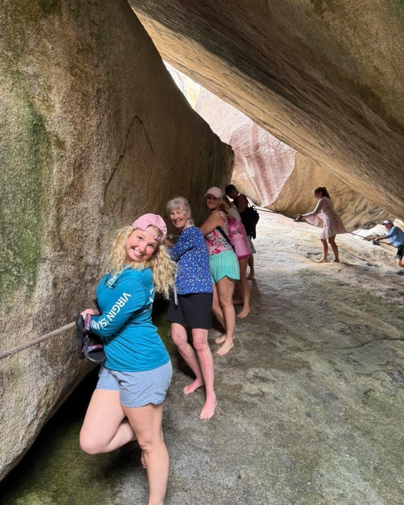 Group of smiling people standing in a narrow rock passage, holding onto a rope.