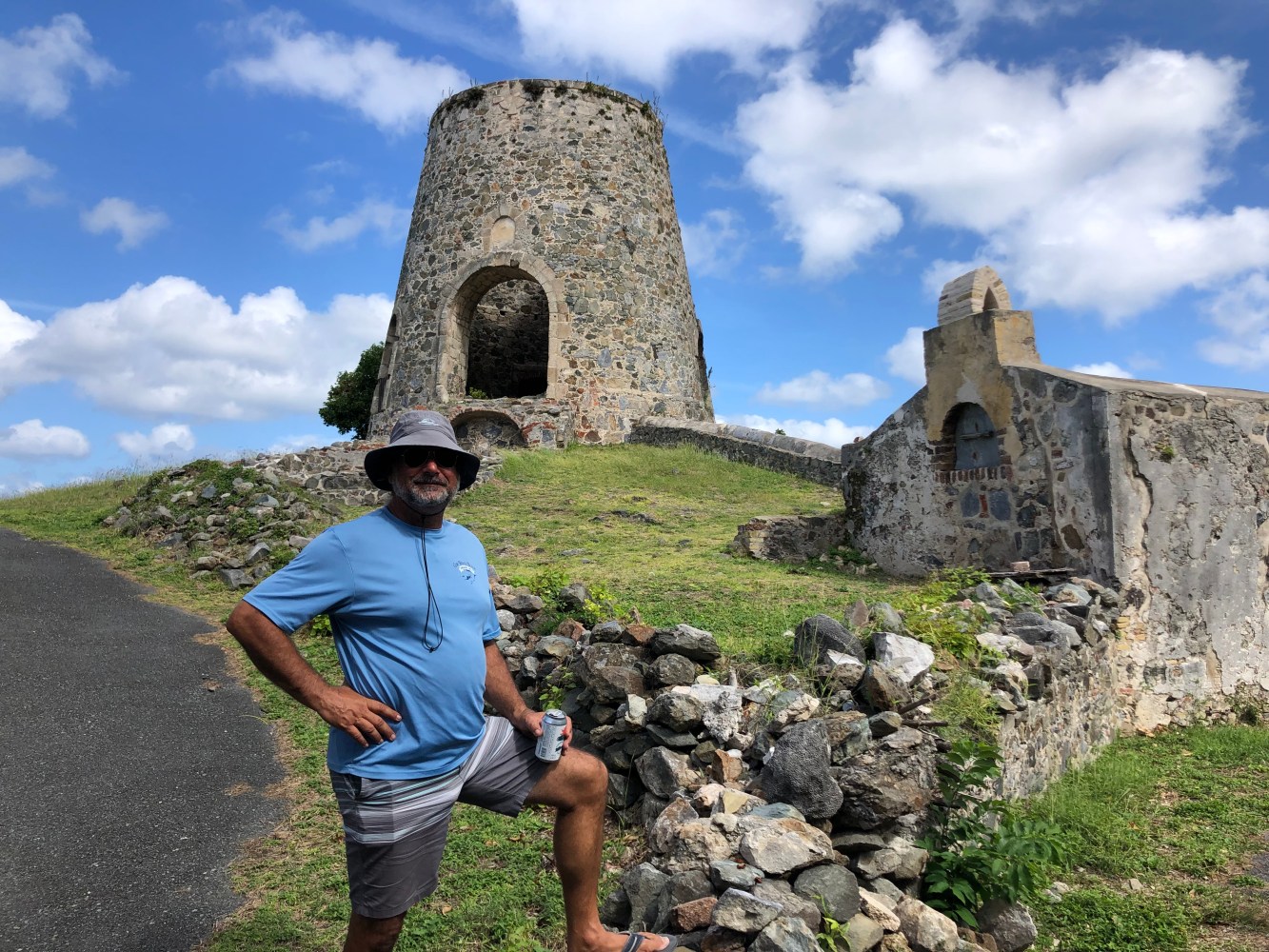 Man in hat stands by stone ruins with tower under blue sky.