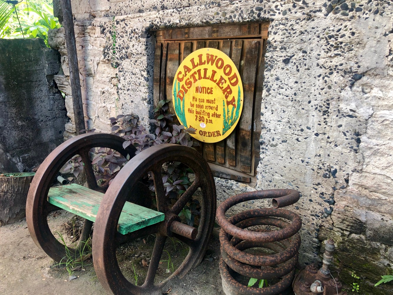 Old distillery sign on stone wall with rusty metal wheels and springs.