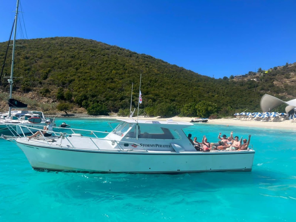 Group on a motorboat in turquoise water near a beach with hills and blue sky in background.