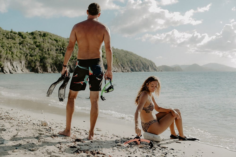 Man and woman on a tropical beach with snorkeling gear.