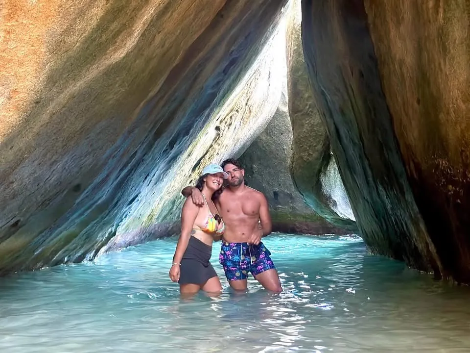 Two people stand in shallow water between large rocks.