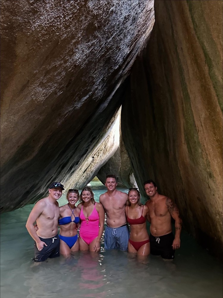 Group of six people in swimsuits standing in a rocky water cave.