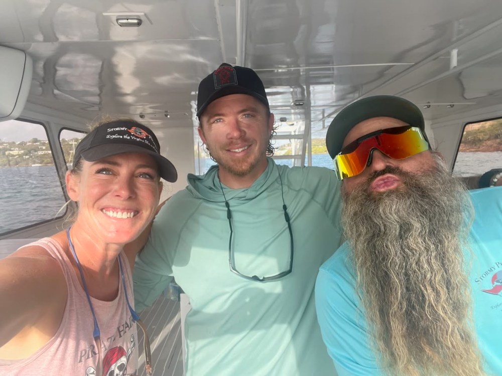 Three people on a boat, smiling; one has a long beard and sunglasses.